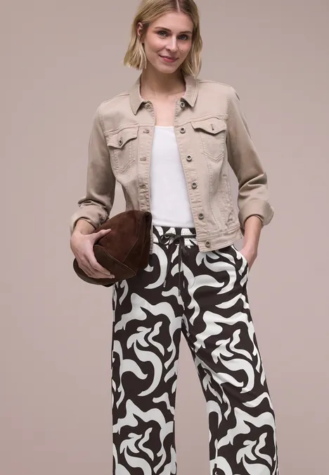 Persoon met zwart-witte motiefbroek, witte top, beige blazer en bruine hoed.