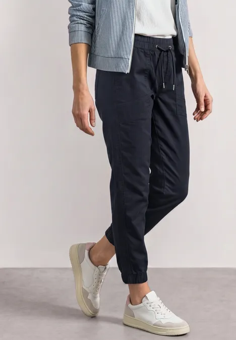 Dames joggerbroek in zwart met elastische enkels, gecombineerd met witte sneakers en een lichtgrijze hoodie.