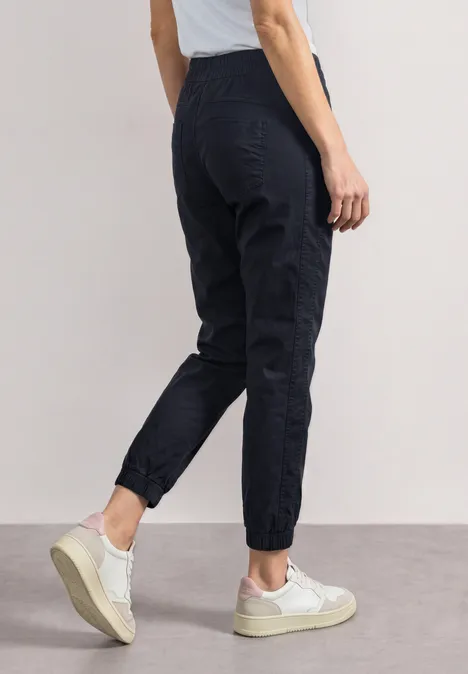 Persoon in zijaanzicht draagt donkerblauwe joggingbroek en witte sneakers voor neutrale achtergrond.