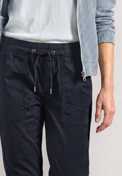 Persoon draagt donkerblauwe joggingbroek met trekkoorden, wit T-shirt en lichtblauwe cardigan.