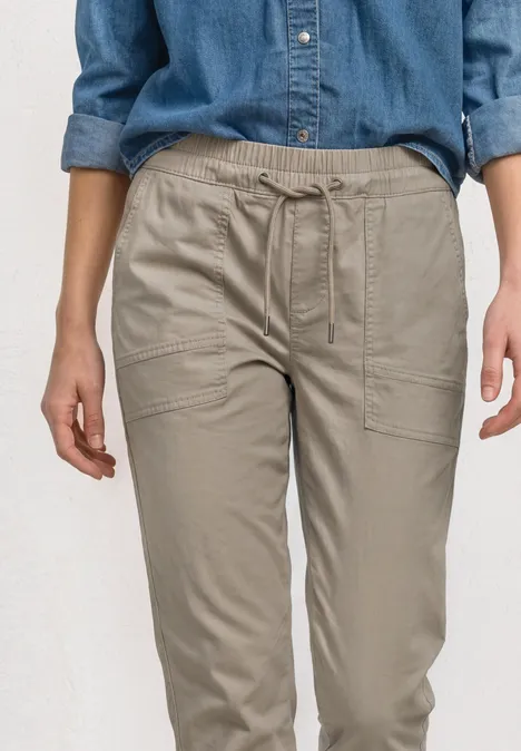 Slim Leg broek in papertouch kwaliteit buff grey Een persoon draagt een comfortabele beige cargobroek van licht materiaal met zijzakken.