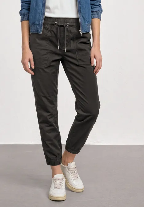 Slim Leg Hose in Papertouch-Qualität deep earth Eine Person trägt dunkle, lässige Jogginghose und weiße Sneaker, nur Beine und Füße sichtbar.