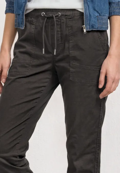 Slim Leg Hose in Papertouch-Qualität deep earth Damen-Jogginghose in dunklem Grau mit Tunnelzugbund und aufgesetzten Taschen, kombiniert mit Jeansjacke