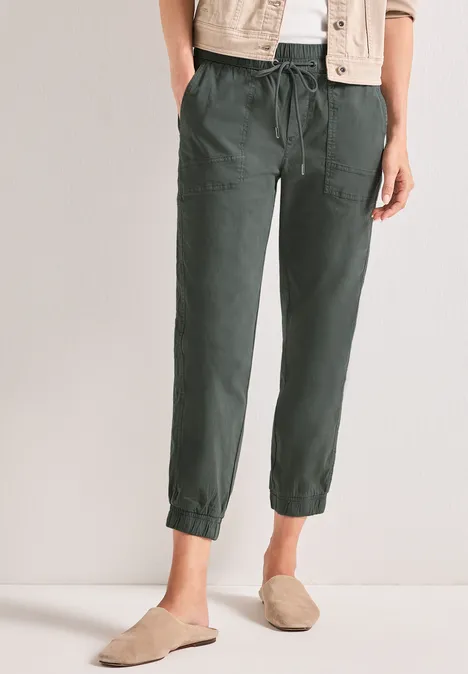 Slim Leg Hose in Papertouch-Qualität cilantro green Damenmodell trägt dunkelgrüne, lockere Leinenhose mit Bündchen am Knöchel und seitlichen Taschen.