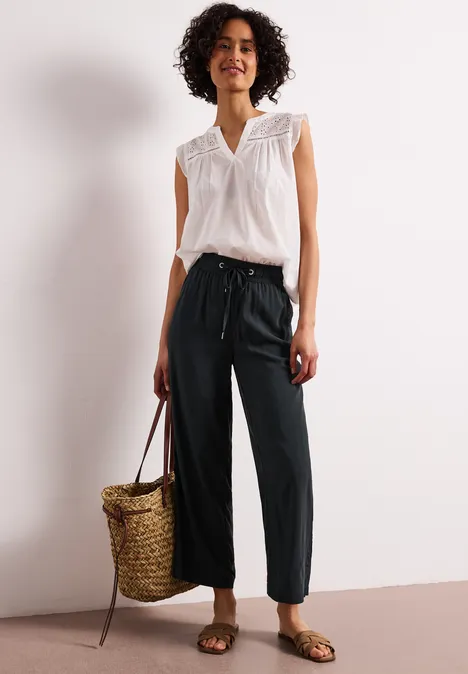 Vrouw in witte mouwloze blouse en zwarte broek met strooien tas.