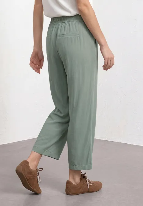 Een persoon draagt losse, groengrijze broek tot de enkels met elastische taille en bruine veterschoenen.