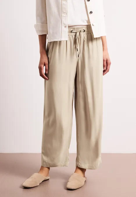 Beige, weit geschnittene Leinenhose mit Kordelzug, dazu helle Pantoletten.