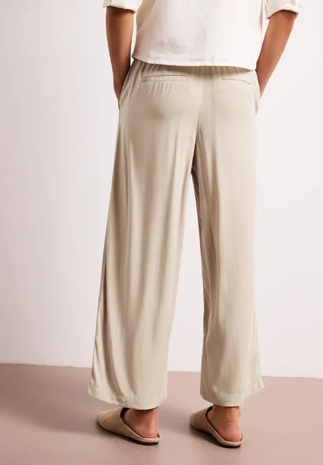 Helle, beigefarbene, locker sitzende, weite Hose mit elastischem Bund und schmal zulaufendem Saum, kombiniert mit Sandalen.