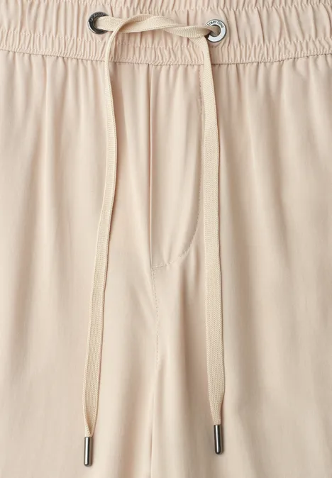 Nahaufnahme eines beigen Hosenbunds mit elastischem Gummizug und beigem Tunnelzug mit Metallösen.