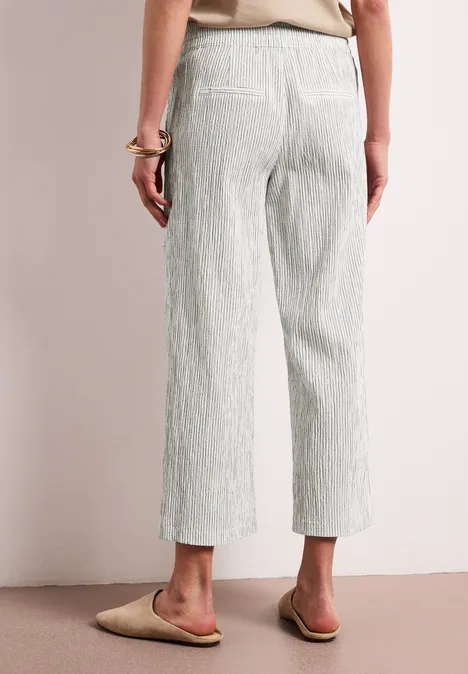 Rückansicht einer Person in hellgrauen, gestreiften Culotte-Hosen und flachen Sandalen.