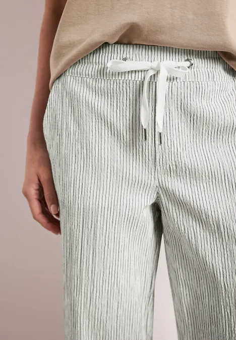 Nahaufnahme einer Person in hell gestreifter Stoffhose mit Tunnelzug an der Taille und beigem Oberteil.