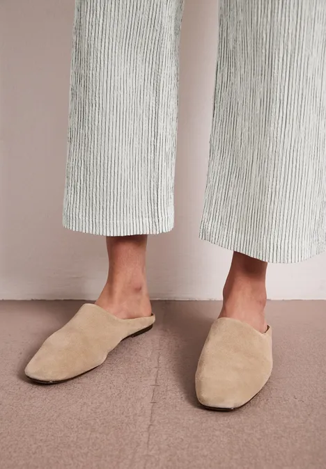 Beige, flache Hausschuhe im Mule-Stil, getragen mit hell gestreifter Hose.