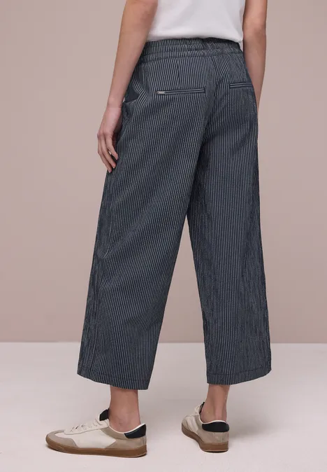 Rückansicht: weite, gestreifte Culottes und weiße Sneaker auf beigem Hintergrund.