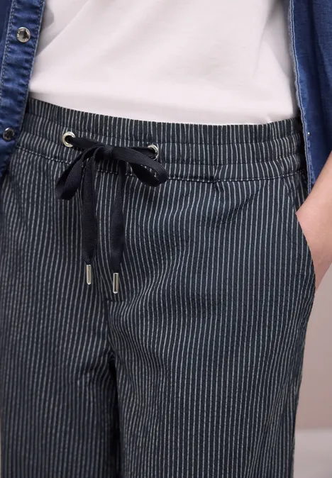 Nahaufnahme einer Person in dunkelblauer, gestreifter Jersey-Hose mit Tunnelzug und Hand in Tasche.