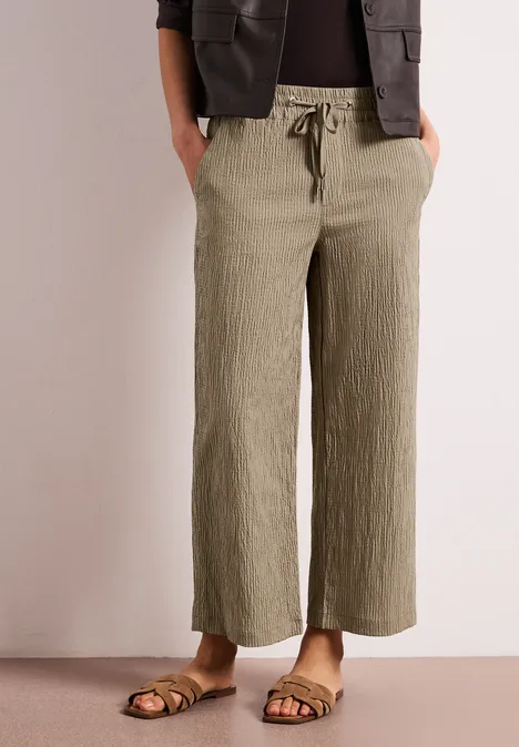 Weite, knöchellange Leinenhose in Olivgrün mit Kordelzugbund und texturierter Oberfläche, kombiniert mit Sandalen.