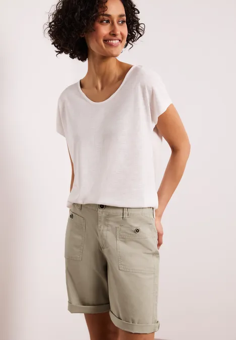 Eine Person trägt ein schlichtes weißes T-Shirt und beige Bermudashorts mit Umschlag und Taschen.