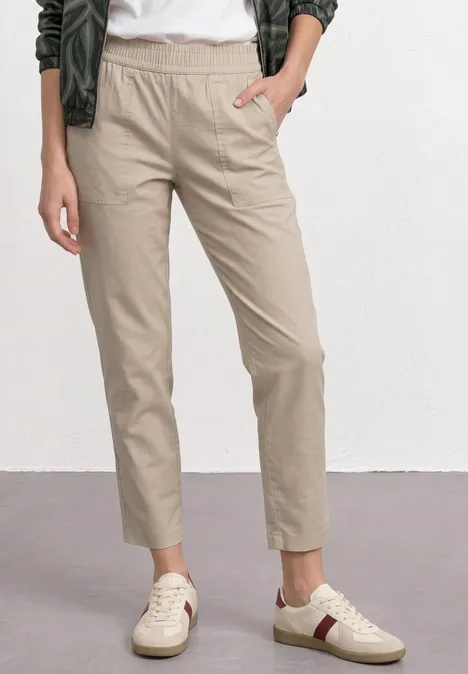 Benen van een persoon in beige chino’s en witte sneakers met kleuraccenten tegen een neutrale achtergrond.