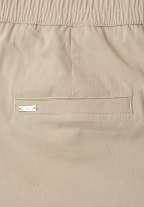 Beige broek met elastische taille en een smalle paspelzak met metalen logo.