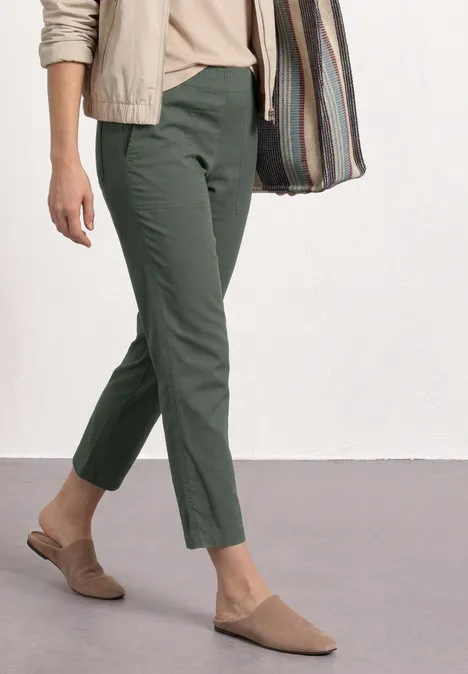 Persoon met olijfgroene broek, beige schoenen en een gestreepte tas.