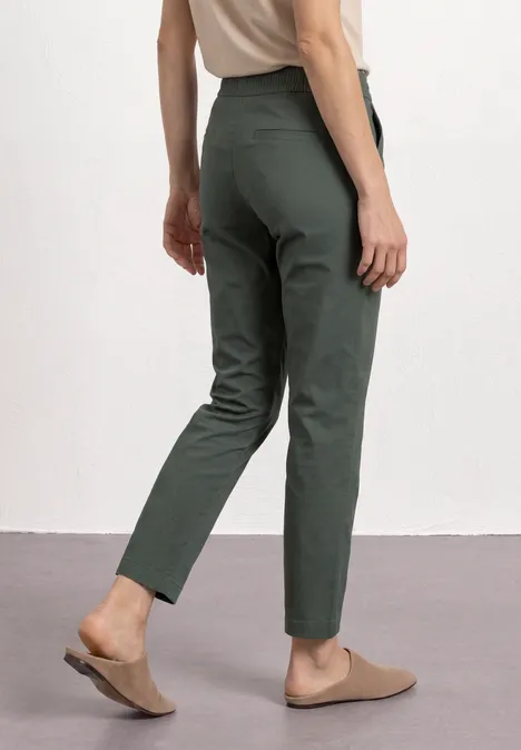 Iemand draagt een groene, slanke broek en comfortabele bruine mules.