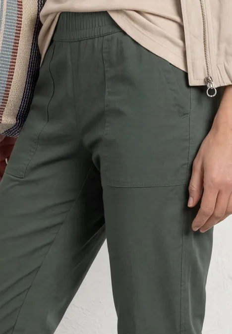 Vrouw met een donkergroene broek en beige top, close-up van het onderlichaam.
