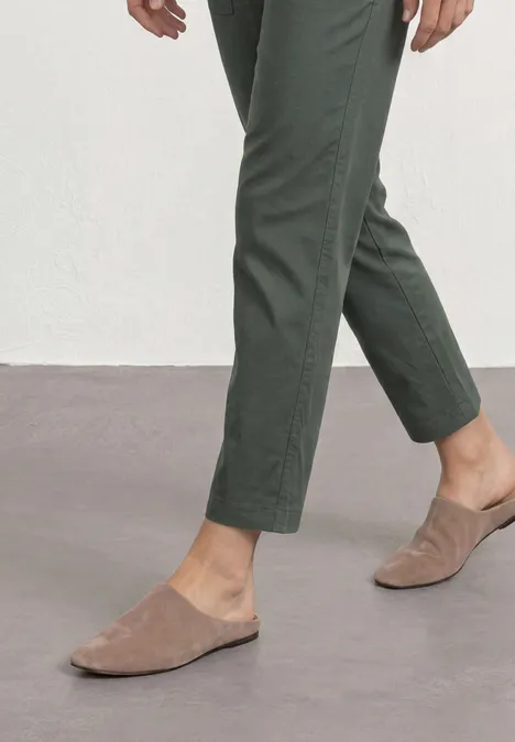Benedenbenen in groene broek en beige suède instappers op grijze vloer