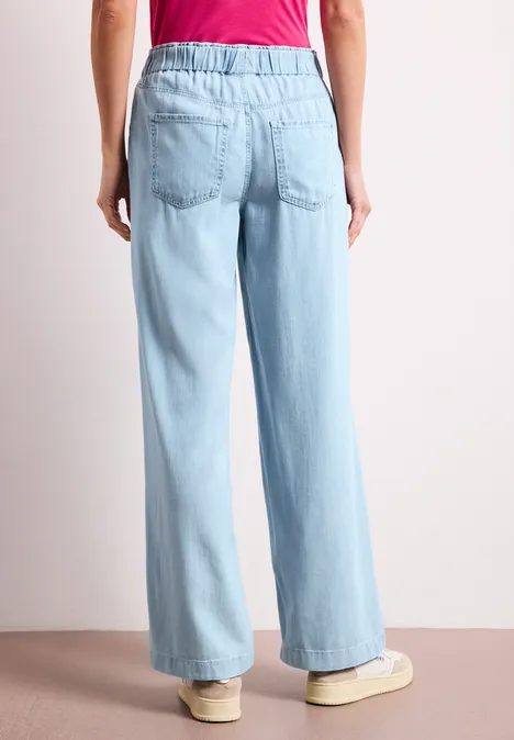 Hinteransicht einer Person in hellblauen, weit geschnittenen Hosen und rotem Oberteil.