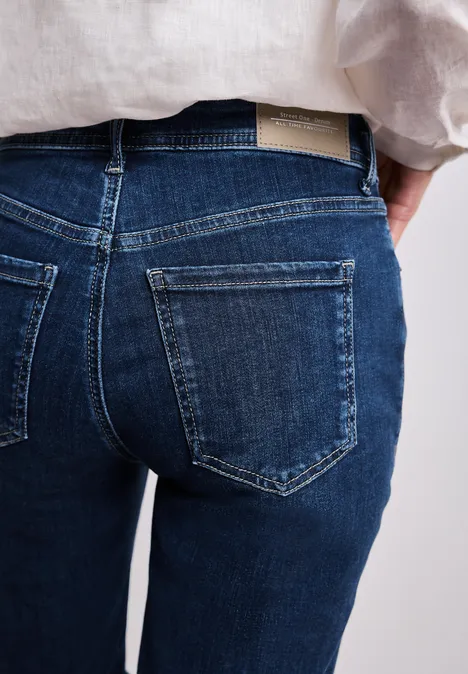 Dunkelblaue Jeans mit zwei aufgesetzten Gesäßtaschen, kombiniert mit einem hellen Leinenhemd.