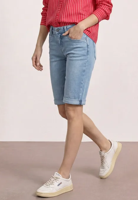 Iemand draagt lichtblauwe denim bermuda met omgeslagen pijpen, witte sneakers en een rood gestreept shirt.