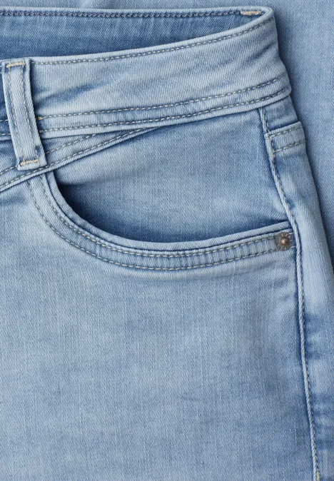 Close-up van een lichtblauwe spijkerbroek met zichtbare voorzak en riemlussen.