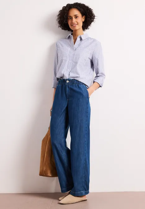 Frau trägt weite Jeans, gestreiftes Hemd und Ledertasche, moderner Casual-Look.