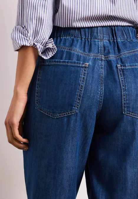 Rückenansicht einer Person in blauen Jeans mit elastischem Bund und gestreiftem Oberteil.