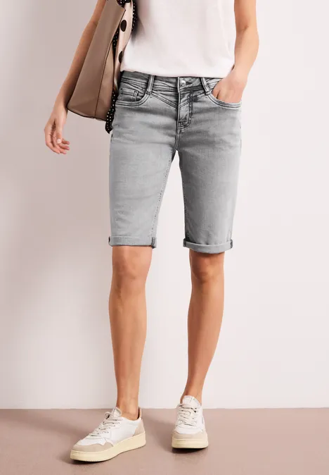 Eine Person trägt hellgraue, kniehohe Jeans-Shorts mit umgekrempeltem Saum, dazu weißes T-Shirt und Sneakers.