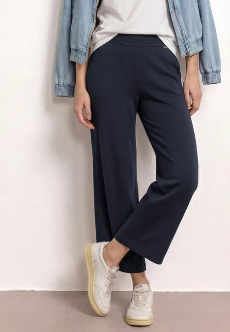 Een persoon draagt zwarte, wijde culottes en witte sneakers.