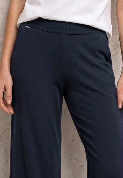 Persoon draagt een wijde marineblauwe broek met zijritszak, losse pasvorm.