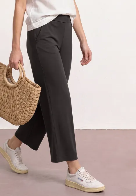 Zwarte 7/8-broek, witte sneakers en gevlochten strozak op lichte ondergrond