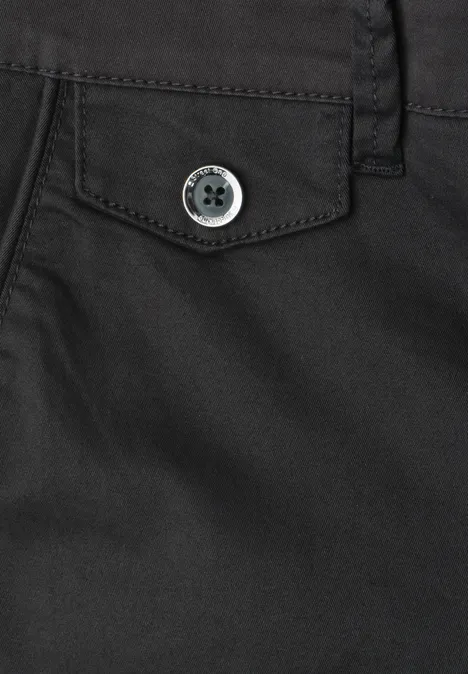 Close-up van een zwarte broek met klepzak en knoopsluiting.