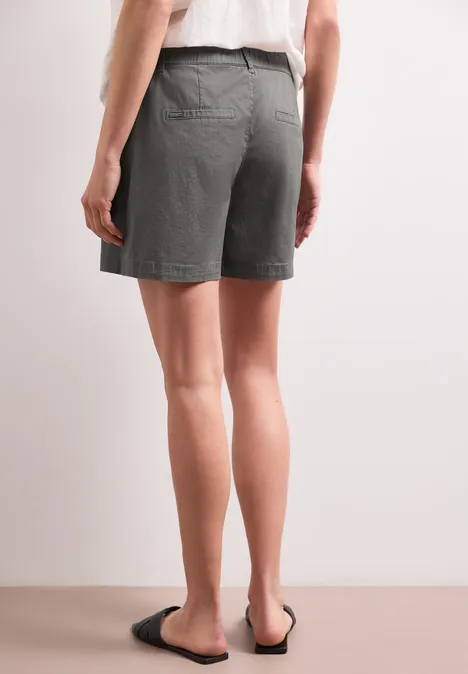 Rückansicht einer Person mit grauen Shorts und schwarzen Sandalen vor neutralem Hintergrund.