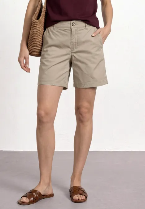 Frau trägt khaki Shorts, braune Sandalen und eine Korbtasche über der Schulter.