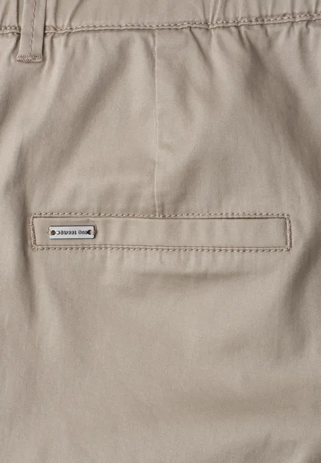 Detailaufnahme einer hellbeigen Hose mit einer verschlossenen Gesäßtasche und dezenter Markenplakette.