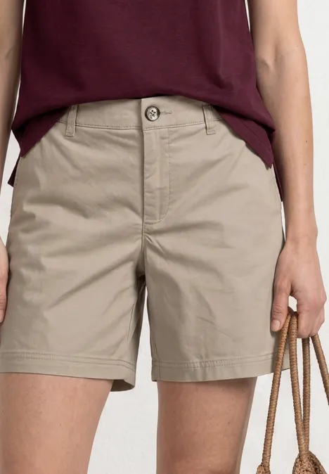 Frau trägt khakifarbene Shorts und bordeauxrotes T-Shirt, hält eine Tasche mit Kordelhenkeln.