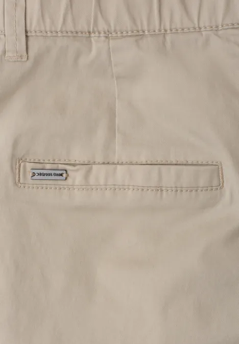 Details van een beige broek met een smalle achterzak en een klein merkembleem.