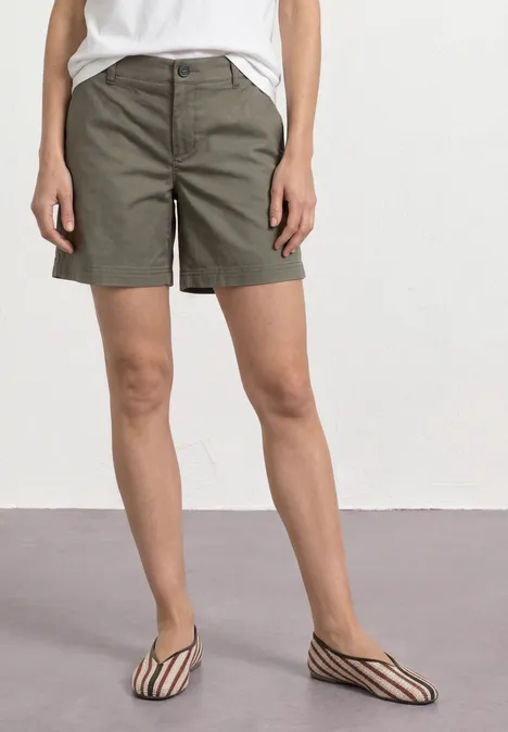 Frau trägt khakifarbene Shorts, weißes Top und schwarz-weiße flache Sandalen.