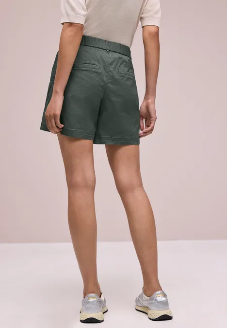 Rückansicht einer Person in schwarzen Shorts, weißem Shirt und Laufschuhen vor neutralem Hintergrund.