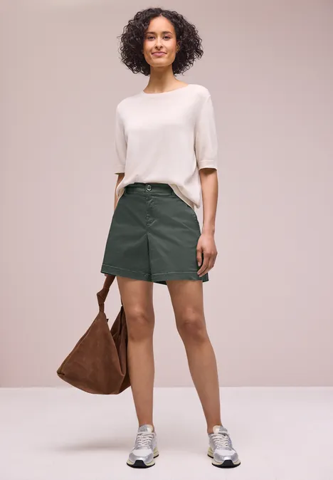 Model trägt weißen Pullover, grünen Rock, Sneakers und braune Tasche