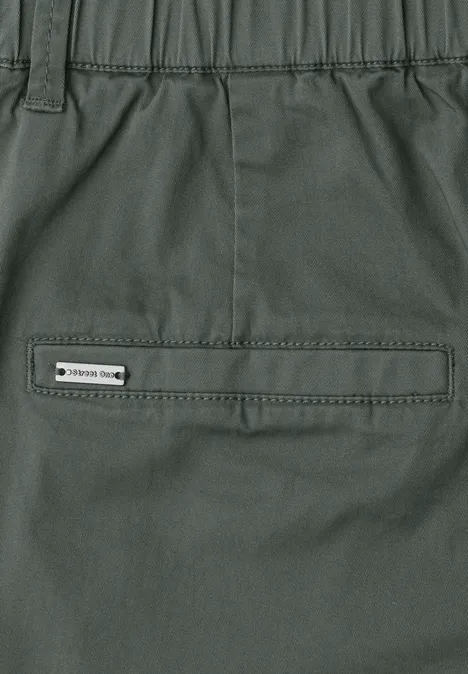 Nahe Ansicht einer olivgrünen Outdoor-Hose mit Reißverschlusstasche und Label am Bund.