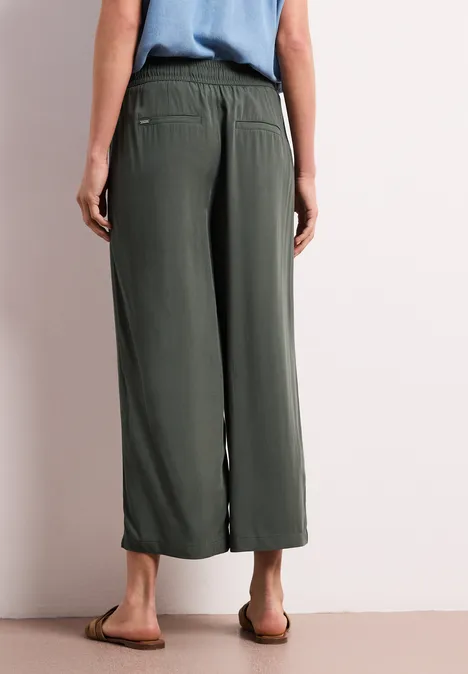 Rückansicht einer Person in olivgrünen, weiten Culotte-Hosen und flachen Sandalen.