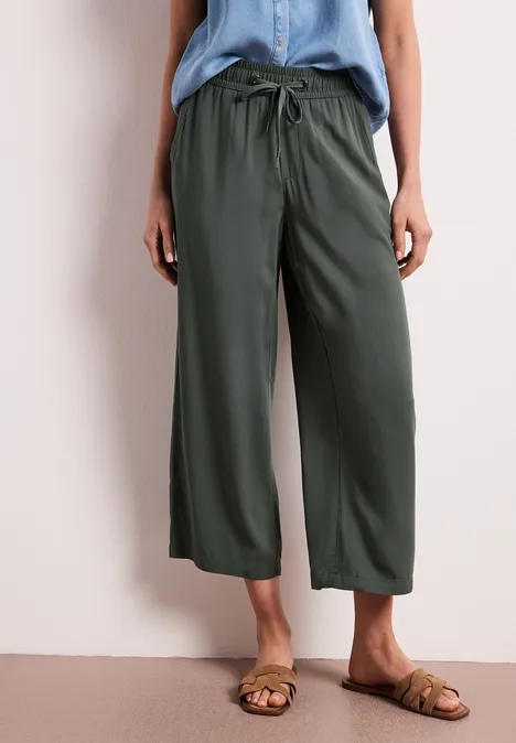 Frau trägt lässige, grüne, weite Culotte-Hose mit Kordelzug und flachen Sandalen.