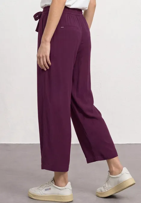 Violette, weit geschnittene Hose mit hoher Taille und Bindegürtel, kombiniert mit weißen Sneakern.