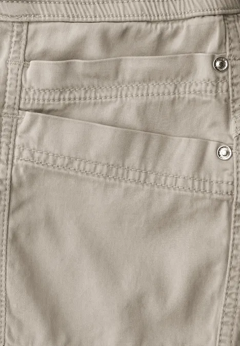 Nahaufnahme einer beigen Hose mit mehreren Taschen und sichtbaren Nähten sowie Druckknöpfen.